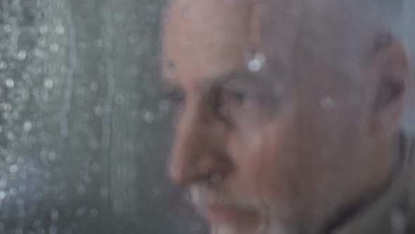 Sad Old Man Looking in Window at Rainy Weather, Pondering About His Life Closeup