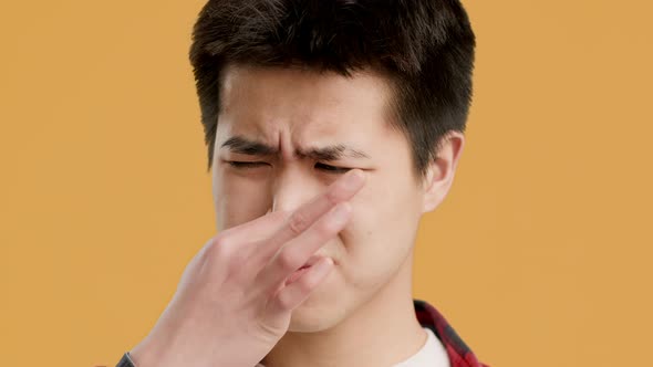 Korean Guy Pinching Nose Feeling Stinky Smell Over Orange Background