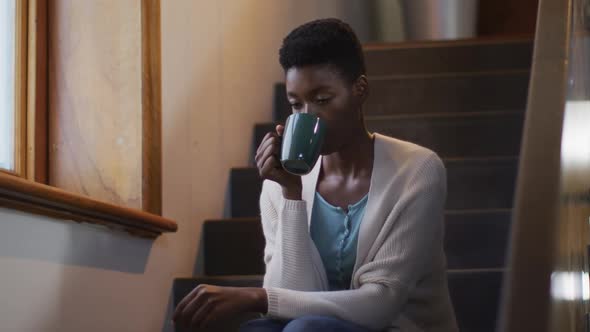 Thoughtful african american attractive woman sitting on stairs an, drinking coffee