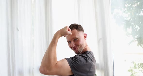 Handsome Man Showing Biceps Against White Curtains