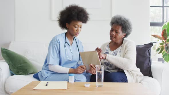 African american female doctor and senior female talking and using tablet
