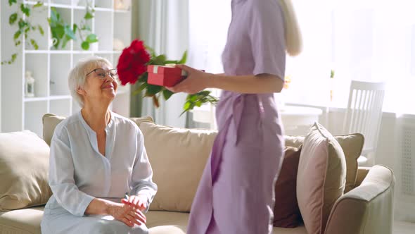 Young woman giving a red flowers to his elderly mother in a home interior