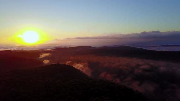 Drone footage of spectacular sunrise over dense forest covered in broken fog. Drone flys forward and