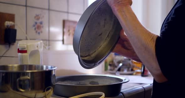 A woman chef coating round baking pans with flour to prevent sticking as she bakes vegan chocolate c
