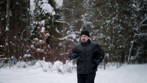 Middleaged Man is Training in Forest in Winter Day Running Over Snow and Breathing Cold Air