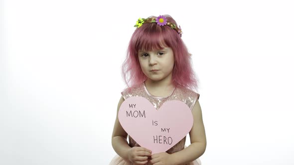 Child Girl Princess Holds Pink Paper Heart with Text About Mother. Mother's Day