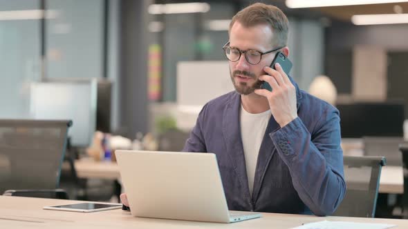 Middle Aged Businessman Talking on Smartphone While Using Laptop