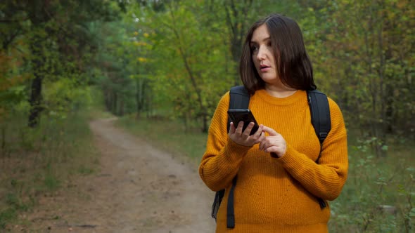 Tired Woman Tourist Reads Map on Phone Walking Along Forest