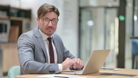 Serious Businessman with Laptop Looking at Camera