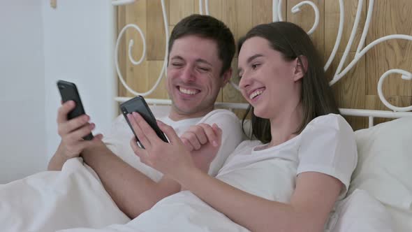 Happy Young Couple Using Smartphone in Bed Together