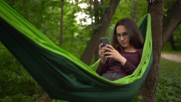 A Young Woman Lies in a Hammock and Communicates on the Internet Through the Phone