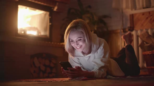 A Pretty Woman Lying Near Fireplace and Having a Video Call