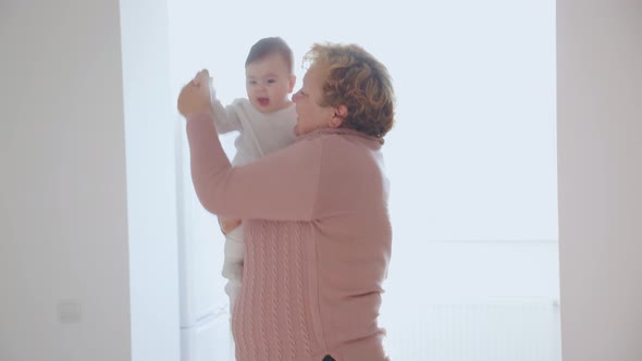 Elderly Woman Holding Her Baby Granddaughter Kiss at Home Young and Old People Together