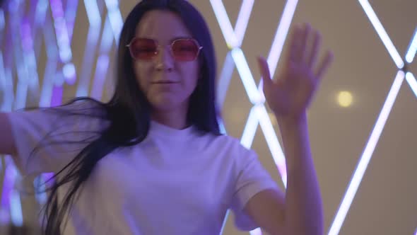 Portrait of Happy Relaxed Caucasian Woman in Sunglasses Dancing in Neon Lights. Cheerful Smiling