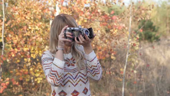 Blonde Girl Takes Pictures on a Retro Camera in Autumn Park