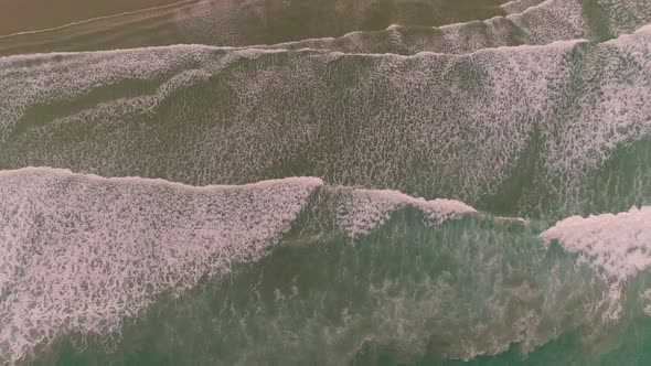 Top down Aerial drone view of waves coming in to the beach. Slow pull up.