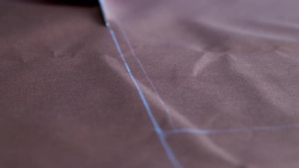 Woman Hands with Scissors Cutting Brown Fabric According to Markings on Tabletop