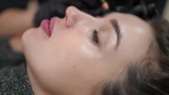 Side View Face of Woman with Blurred Hand Forming Eyebrows at Background for Permanent Makeup