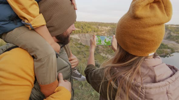 Family of Three Looking at Map on Mobile Phone Outdoors