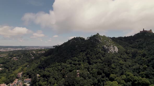 Aerial panning shot of Sintra Hills against beautiful cloudscape and Pena palace