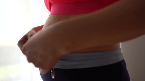 Closeup of a Pregnant Woman in a Red Sports Top and Leggings Measuring Her Waist with a Tape Measure