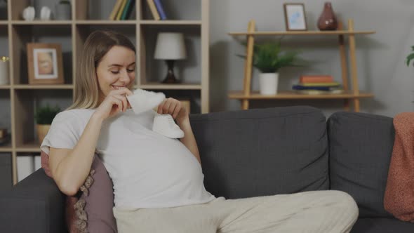 Pregnant Woman Sitting on Couch with Baby Shoes in Hands