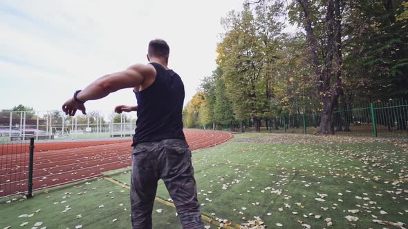 Male fitness sportsman training his body on the stadium. Muscular man dressed in black shirt exercis