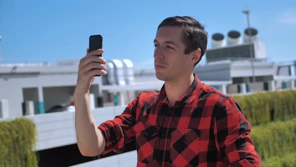 Smiling Young Man Talking Cellphone Using Video Communication Outside on the Roof