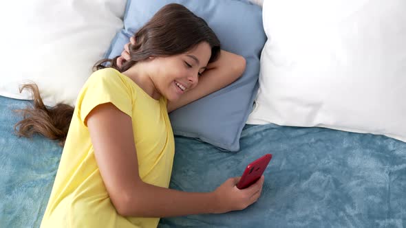 Cheerful Teen Girl Texting Message on Phone in Bed Blogging