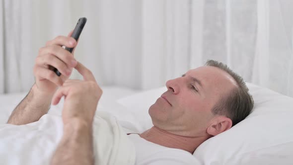 Relaxed Middle Aged Man Using Smartphone in Bed 