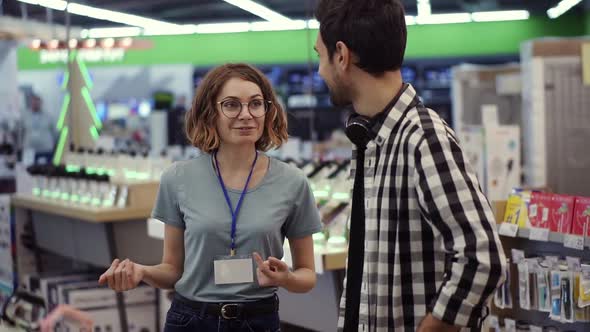 In the Electronics Store  Positive Female Consultant Gives Professional Advice to a Young Man