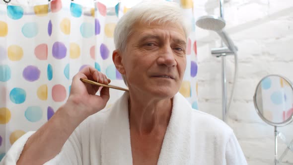 Senior Man in Bathrobe Combing Hair in Bathroom in Morning