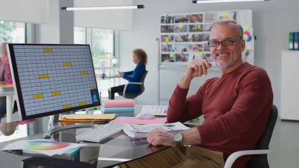 Portrait of Smiling Senior Businessman Sitting at Desk in Modern Office and Smiling at Camera