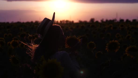 Young Woman with Long Hair and Straw Hat in a Beautiful Field of Sunflowers at Sunset Time