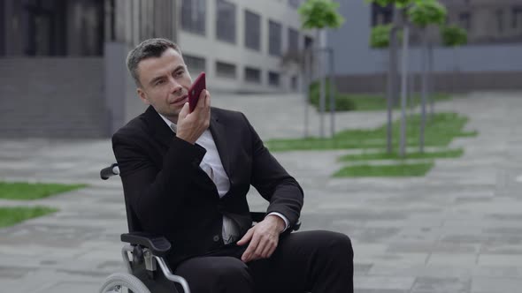 Successful Man in Suit Using Smartphone While Sitting in Wheel Chair at Street