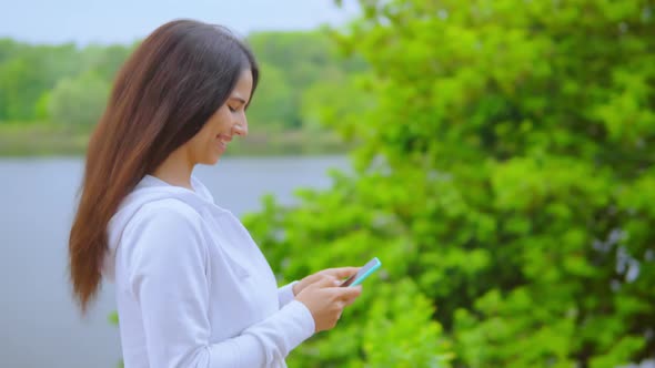 Side View on the Girl Using Smartphone Walking Along River