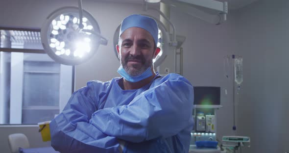 Portrait of caucasian male surgeon wearing lowered face mask smiling in operating theatre
