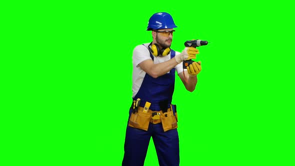 Builder Holds a Drill in His Hands and Looks Around. Green Screen