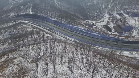 Drone Flight Over a Winter Forest and a Highway Among the Hills