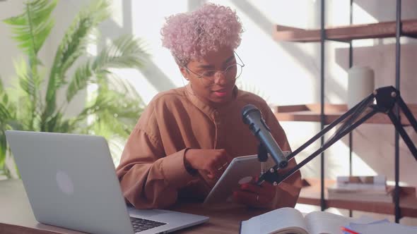 Woman in Front of a Microphone Reads on a Digital Tablet During a Podcast