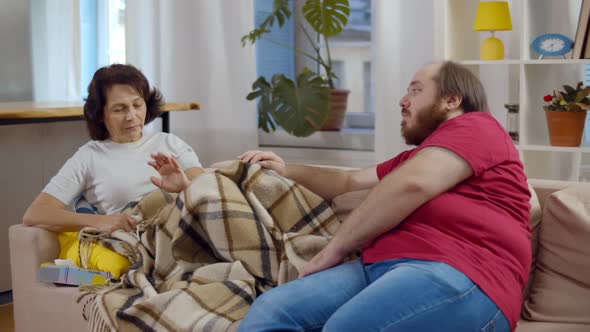 Young Overweight Man Taking Care of His Sick Mom Sitting Together on Couch