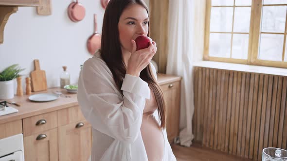 Pregnant Woman Enjoys Eating Fresh Ripe Apple in Kitchen