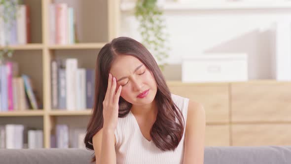 Asian woman sitting on sofa have a headache and Migraine feeling so stressed