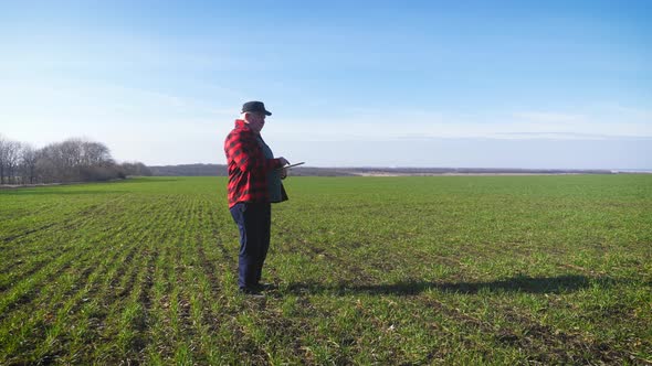 Senior Agronomist Man Looks at a Fresh Green Field After Winter. Smart Farming, Using Modern