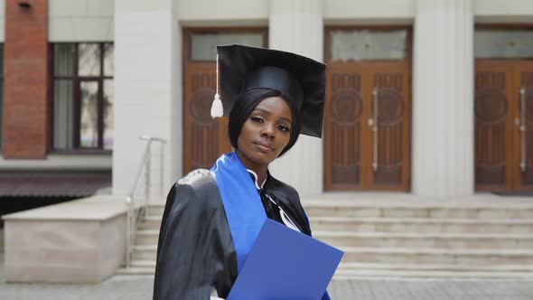 African American Female Graduate in Black Gown and Square Master's Hat Holding Diploma on University