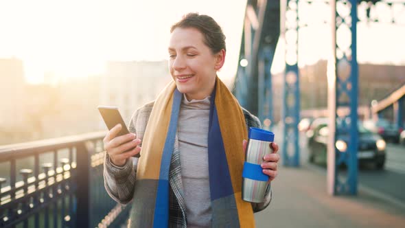 Caucasian Businesswoman in a Coat Walking Across the Bridge on a Frosty Morning Drinking Coffee and