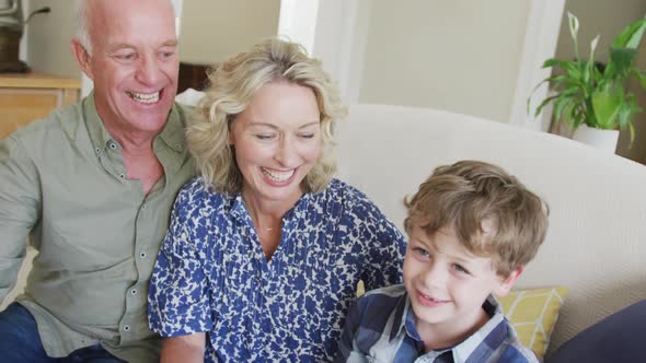 Happy caucasian grandparents with grandson taking selfie and sitting in living room