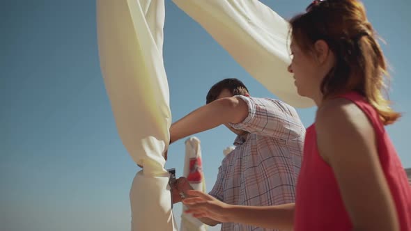 Caucasian Decorators Draping Wedding Arch Near Sea with Staple Gun in Slowmotion