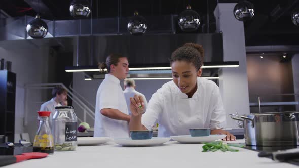 African American female chef wearing chefs whites in a restaurant kitchen seasoning food