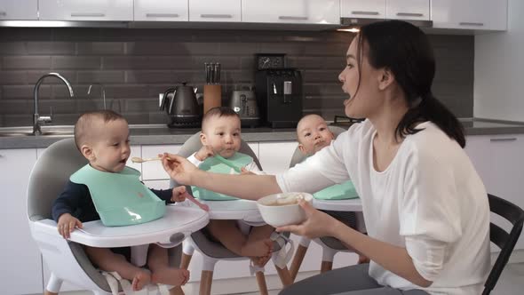 Asian Mom Feeding Puree to Sloppy 1-Year-Old Triplets